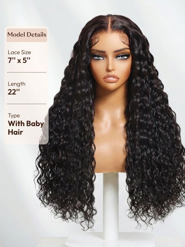 A 22-inch dark wig with tight, voluminous curls is displayed on a stand. Fine baby hairs and a sheer lace front create a realistic, soft-looking hairline.