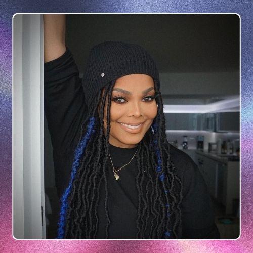 Janet Jackson wearing a black beanie with long blue faux locs hairstyle