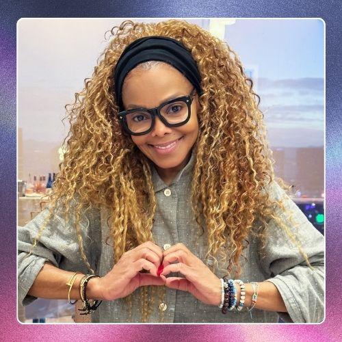 Janet Jackson with blonde curly hair wearing glasses and a black headband