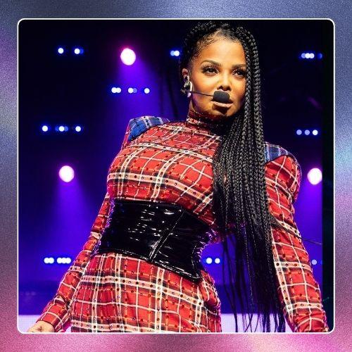 Janet Jackson performing on stage in a red plaid outfit with long braided hair