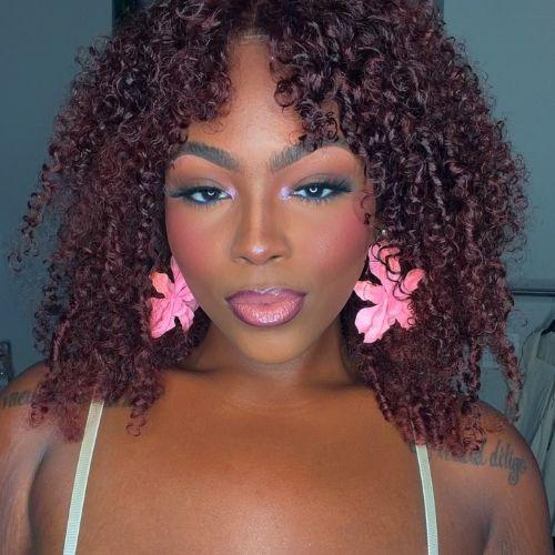 Close-up of woman wearing a curly reddish-brown wig and pink earrings