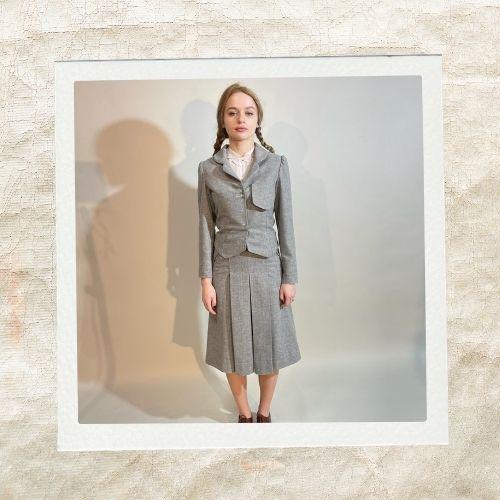 Joey King wearing a grey double-breasted skirt suit with a long neat braid hairstyle