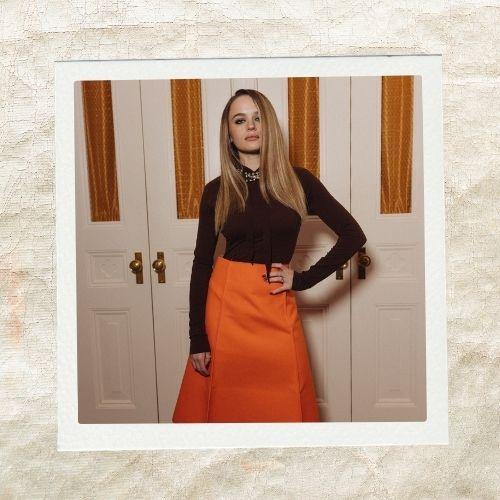 Joey King wearing a turtleneck and bright orange skirt with long sleek straight blonde hai