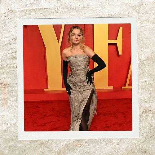 Joey King in a strapless gown and long black gloves with a chic messy low bun hairstyle