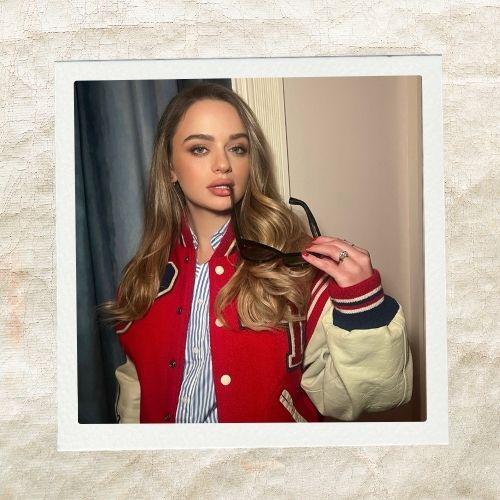 Joey King wearing a red and white varsity jacket with styled golden-blonde wavy hair