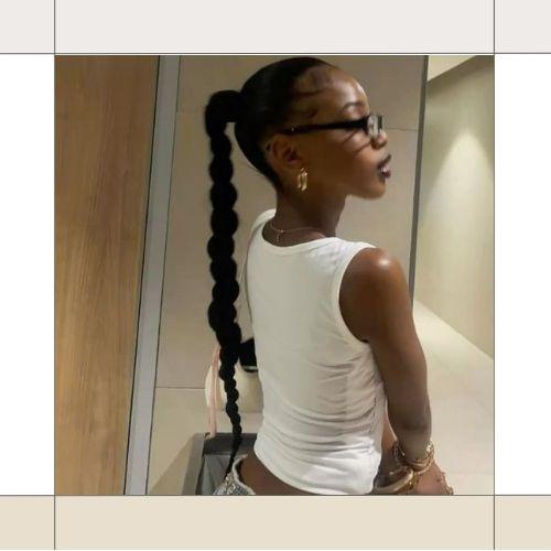 Woman showing a long feed-in braided ponytail hairstyle wearing a white tank top