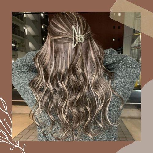 Half-up hairstyle with ash blonde ribbon highlights on wavy brown hair
