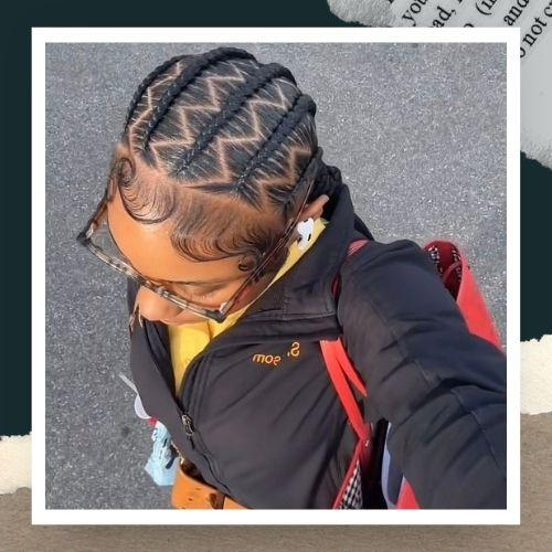 A woman wearing glasses and a jacket with zig-zag parted cornrow braids.