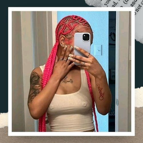 A woman taking a selfie in a white tank top showing bright pink-dyed cornrows.