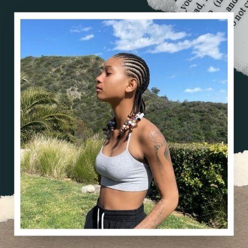 A woman outdoors wearing a white crop top with bead-adorned cornrow braids.