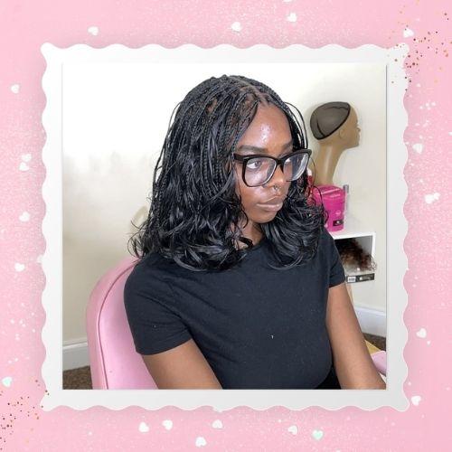 A woman with glasses and dark french curl boho bob braids wearing a black shirt.