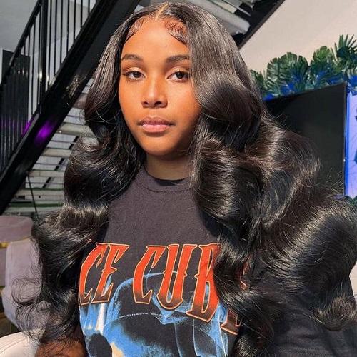 A woman wears black human hair body wave bundles styled in a middle part with full, glossy curls.
