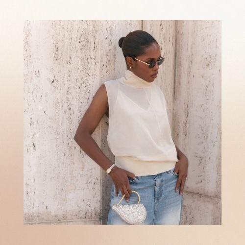 Ryan Destiny with a slicked-back bun, wearing a white sleeveless top and sunglasses.