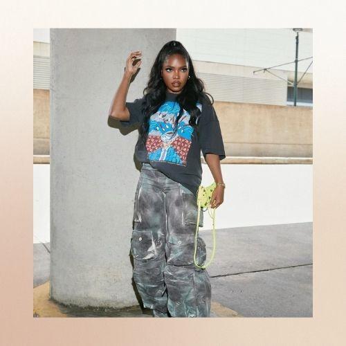 Ryan Destiny in a half-up half-down hairstyle, wearing a graphic tee and maxi skirt.