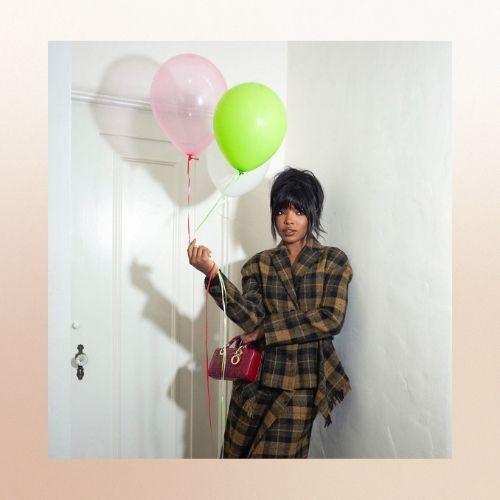 Ryan Destiny with bang hair, wearing a plaid outfit and holding balloons.