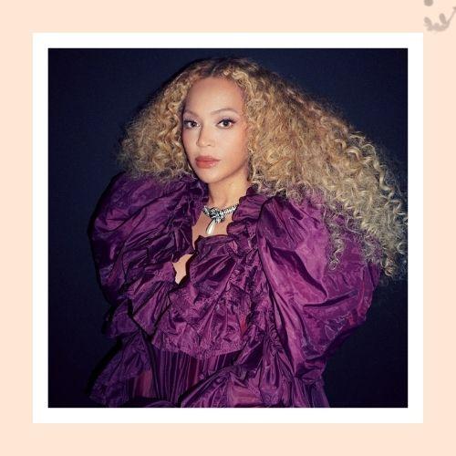 Beyoncé with voluminous afro-textured blonde curls wearing a purple ruffled dress
