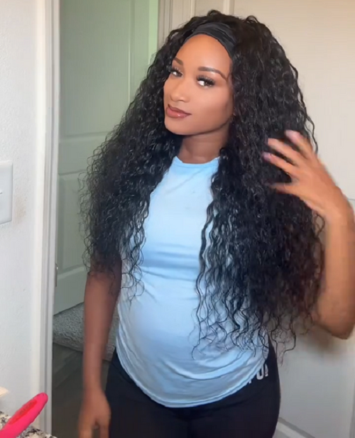 A woman in a light blue t-shirt displaying a long wavy headband wig.