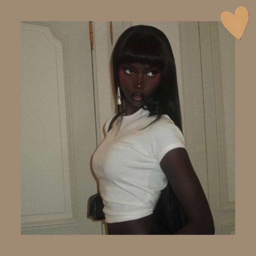 Anok Yai with long straight hair and blunt bangs in a white top