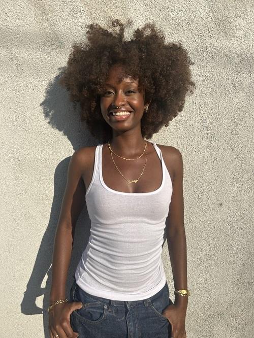 A smiling woman with 4c natural hair wearing a white tank top